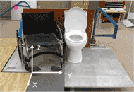 A manual wheelchair is placed adjacent to the left side of a commode on a transfer station. The transfer station includes three force plates, which are placed underneath the wheelchair, the toilet, and the subject’s feet, and two 6-component load cells, each attached to a steel beam used to simulate an armrest of the wheelchair and a grab bar next to the toilet.